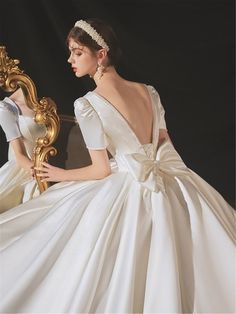 a woman in a white dress sitting on a chair with a golden mirror behind her