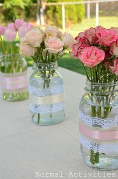 three vases with pink and white flowers in them sitting on a table near grass