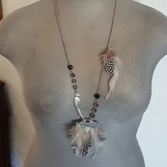 a mannequin wearing a necklace with feathers on it's neck and beads hanging from the chain