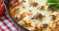 a casserole dish with meatballs, cheese and tomatoes on a tablecloth