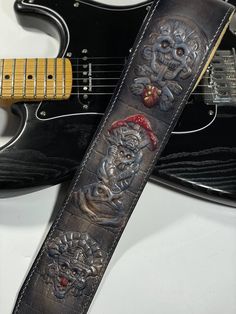 the guitar strap has two skulls on it and is next to a black electric guitar