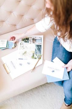 a woman is sitting on a couch with some books and pens in her hand as she looks at photos