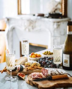 an assortment of cheeses, meats, and fruit on a table next to a bottle of wine