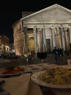 two plates of food are on a table in front of an old building at night