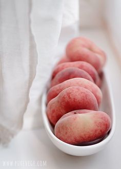 a white bowl filled with peaches sitting on top of a table next to a napkin