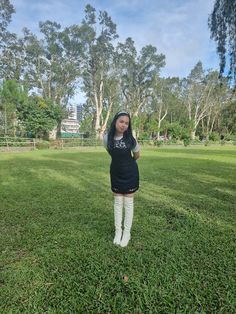 a woman standing in the grass with her arms up and hands behind her head, wearing white knee high socks