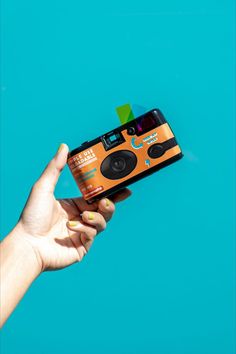 a hand holding an orange and black camera on top of a blue background with the lens up