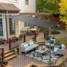 an outdoor living area with couches, tables and umbrellas on the deck in front of a house