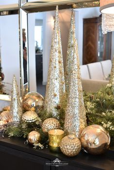 christmas decorations on a mantle in front of a mirror and tree with gold baubies