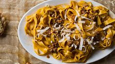 a white plate topped with pasta covered in meat and cheese next to bread on a wooden table