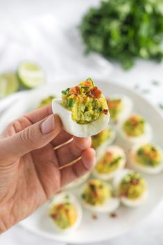 a person holding an open deviled egg on a plate with other deviled eggs in the background