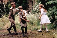 three children are playing in the woods with one pointing at something while the other looks on