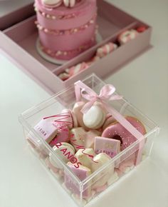 two boxes filled with pink and white candies on top of a table next to a cake