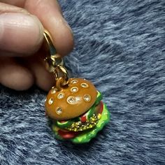 a hand holding a hamburger shaped charm on a blue furnishing surface with a gold plated key chain hanging from it's end