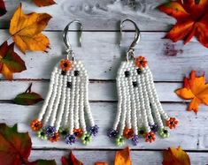 two white beaded ghost earrings with flowers and beads hanging from them on top of leaves