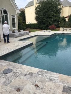 a man standing in front of a pool next to a house with a stone patio