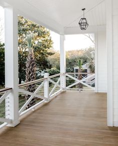 a porch with wooden floors and white railings on the side of it, leading to trees