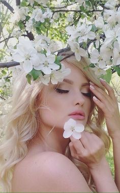 a woman with long blonde hair and white flowers on her head is standing under a tree