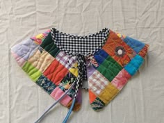 a multicolored patchwork vest with two knitting needles on the bottom and one needle in the middle