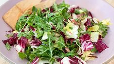 a purple bowl filled with green and red salad