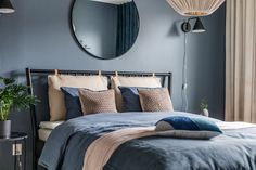 a bed with blue sheets and pillows next to a round mirror on the wall above it