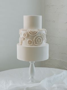 a three tiered wedding cake with pearls on the top and bottom is sitting on a white tablecloth