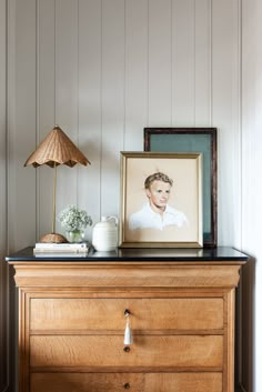 an old dresser with a portrait on top and a lamp next to it in the corner