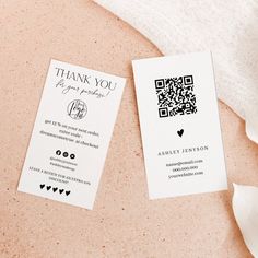 two white business cards sitting on top of a pink tablecloth next to a flower