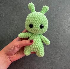 a hand holding a small green crocheted stuffed animal with black eyes and ears