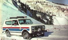 an old police car is parked on the side of a snow covered hill with mountains in the background