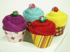 four cupcakes with colorful frosting and candies on top are sitting next to each other