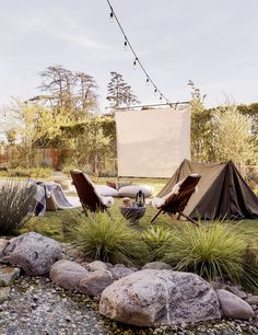 two lawn chairs sitting in the grass next to a movie screen and some rocks on the ground