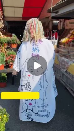 a woman with dreadlocks is walking down the street in front of some vegetables