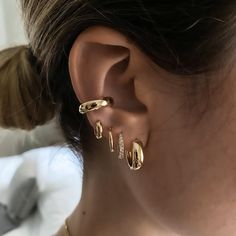 a woman wearing three different types of ear piercings on her left ear and the other one is gold