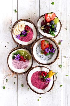 four coconut bowls filled with different types of food on top of a white wooden table