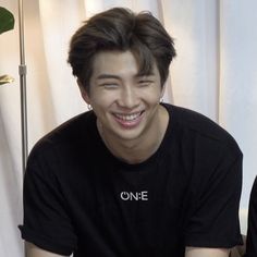 a young man smiling while sitting in front of a white curtain with his eyes closed