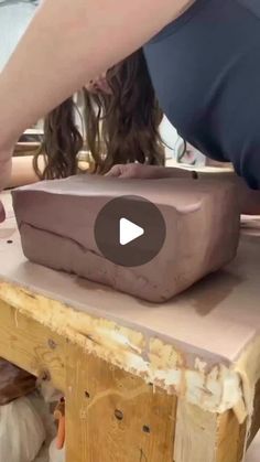 a woman is making something out of clay on a wooden table with other people around her