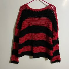 a red and black sweater hanging on a clothes hanger next to a white wall