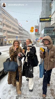 three women are walking down the street in the snow and one is eating an apple