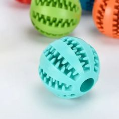 four different colored balls with holes in them on a white surface and one is green, the other is orange