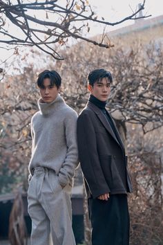 two young men standing next to each other in front of some bare trees with no leaves