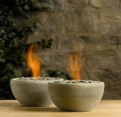 two stone bowls sitting on top of a wooden table next to a brick wall and fire