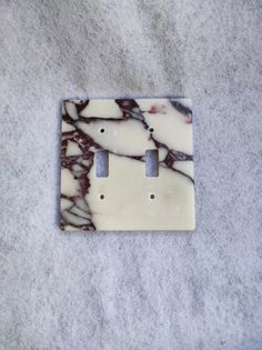 a marble light switch plate cover sitting on top of a white carpeted floor next to an electrical outlet