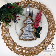 a crocheted christmas tree on a plate next to holly branches and red berries