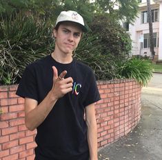 a young man standing next to a brick wall giving the peace sign with his hand