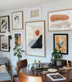 a dining room table with chairs and pictures on the wall above it, along with potted plants