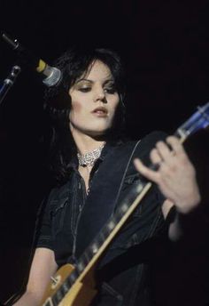 a woman holding a guitar while standing in front of a microphone