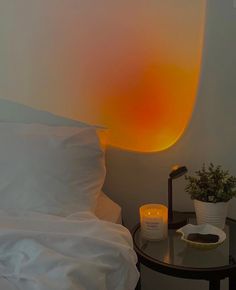 a bed with white sheets and pillows next to a table with a lit candle on it