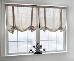 a window with two curtains hanging on it's sides and a candle holder in front of the window