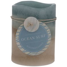 an ocean surf scented candle with a blue lid and white flower on the top, sitting in front of a white background